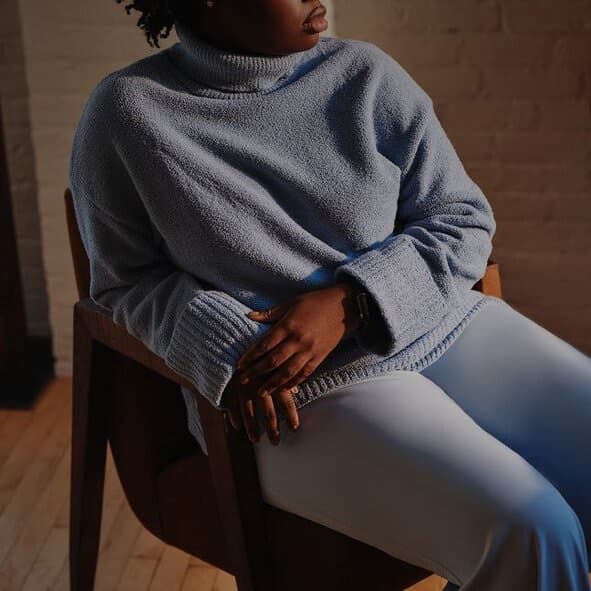 A woman in a blue sweater sitting alone in a chair, looking away